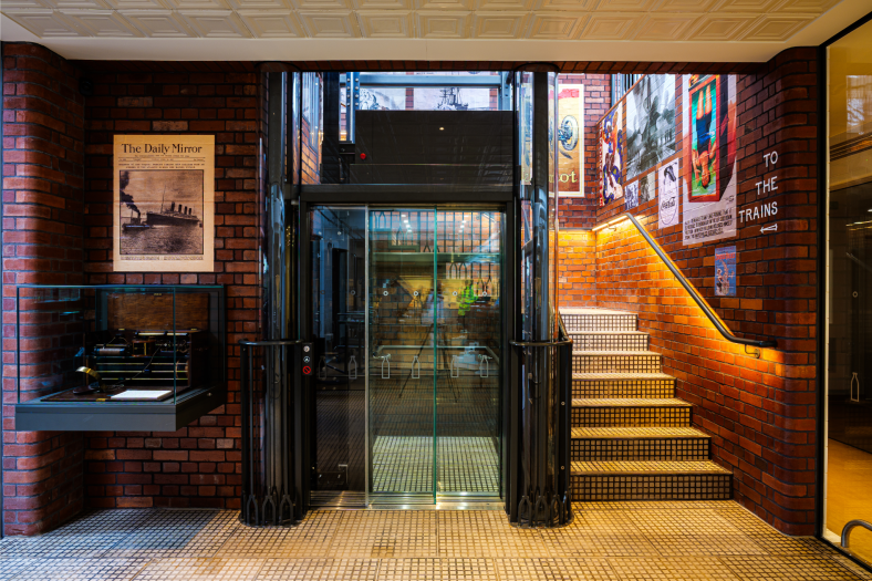 View of bespoke glass lift at ground level in train-themed cafe and cheese factory, The Creamery in Somerset